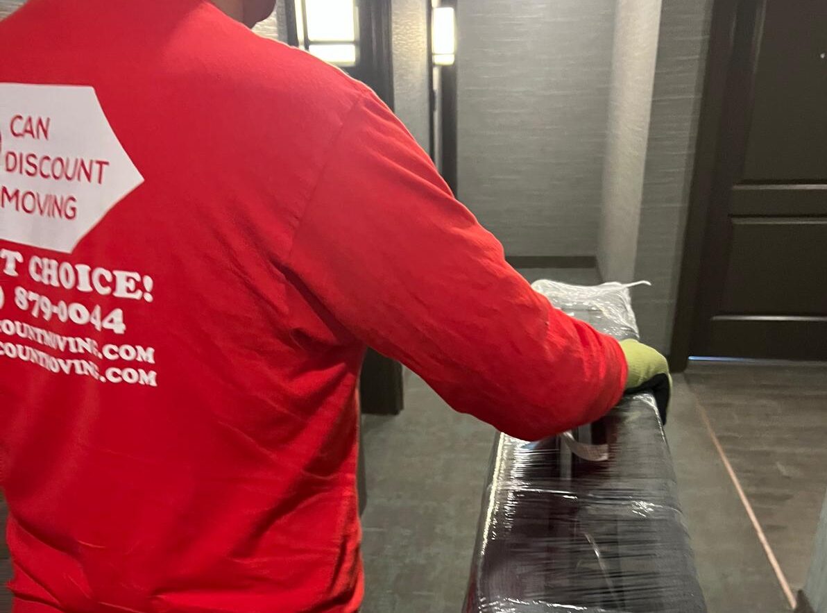 Moving company worker carrying sealed boxes and carefully placing furniture inside a new home during relocation